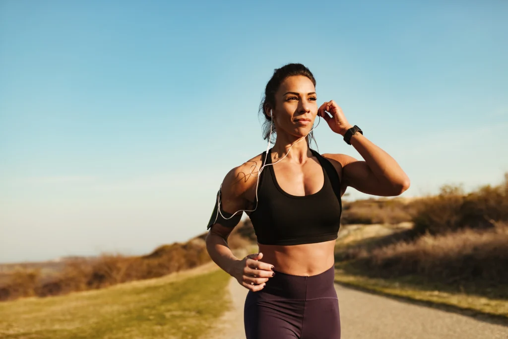 Young, athletic woman running on an outdoor trail while adjusting her earphone.